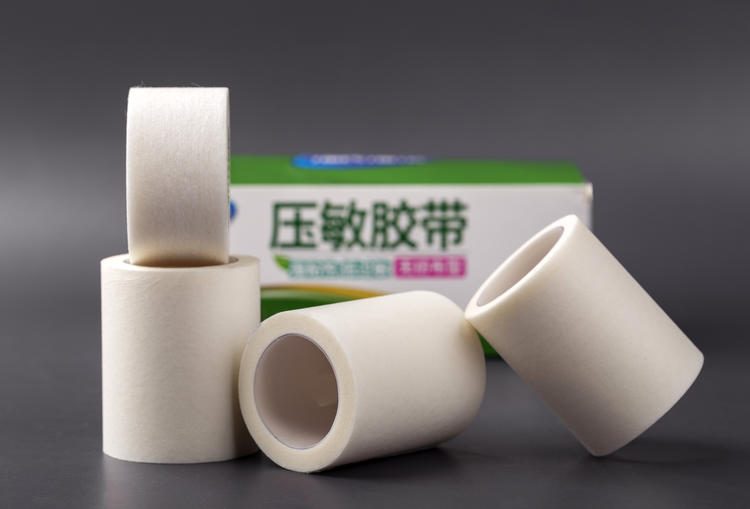 多卷白色医用胶带卷堆叠,背景可见「压敏胶带」包装盒;剥离力报告的测试对象是成品卷,核对报告上的角度、速度等条件要素
